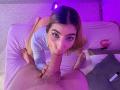 SecretLoversVIP is giving a blowjob to a guy with a huge, hairy, erect cock. She's on her knees, wearing a light blue top, with purple lighting in the background.