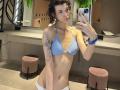 ErynAttridge takes a selfie in a mirror, wearing a blue and white bikini, exposing her toned physique and floral tattoo on her right arm. She has wet, curly hair and a blue wristband.
