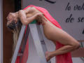 SheylaSpooner is hanging off a ladder with a neon pink sheet covering her ass and tits, her long blonde hair flowing, and her red-painted nails gripping the green step.