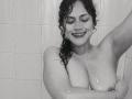 Black-and-white photo of IvannaDuran, smiling with eyes closed, wet curly hair, holding her large, bare, dripping wet tits in a shower, water droplets on her skin.