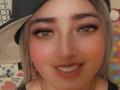 AlessadraJoness has blonde hair, a black cap, green eyes, thick eyebrows, a nose piercing, and a forehead gem. She's smiling with makeup and a gold necklace.