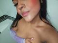 SheilaBrunette with pink blushed cheeks, black hair, and a slight smile, holding her bare tits with a purple top pulled down, visible nose piercing, and pink lipstick.