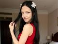CherelleGess with long black hair, wearing a red sleeveless top, white butterfly hair clips, and smiling slightly, holding her hair. Her tits are small and her ass is unseen.