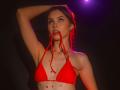 AgataRyili with red bikini top, holding strings in mouth, arm raised, tattoos on chest, red earrings, purple light, dark background, looking up, slight smile, red hair.