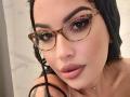 ZoeyMarie with wet black hair, tortoiseshell glasses, and drooling pink lipstick, has a thin strand of saliva hanging from her lower lip. She's wearing a delicate necklace.