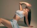 VirgieCrotts is crouching with her back arched, head tilted back, and arm raised. She's wearing a light blue sports bra and skirt, showing her tits and ass.
