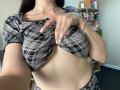 OliviaGranda lifting her plaid shirt to expose her bare tits, showing her flat stomach and a silver bracelet on her right hand. Her nails are long and white.