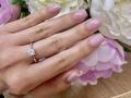 OliviaGrandas Hand mit glänzenden rosafarbenen Nägeln, einem zarten rosafarbenen Ring und einem funkelnden Diamantring, ruht auf weißen und rosafarbenen Blumen..