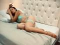 IsabellaaSmith lies on a bed, wearing teal lace lingerie, with her tits and ass exposed, legs crossed, and a red anklet, arms above her head, eyes closed.