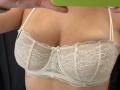 MargoFun's white lace bra covers her tits, featuring intricate floral patterns and thin straps. Her hand holds a green phone, partially in frame, above her chest.