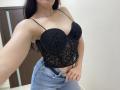 OliviaGranda with black lace-up bra showcasing her tits, wearing blue jeans, holding her waistband, long dark hair, necklace, and a bracelet, in a bathroom setting.