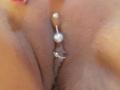 Französisch: Shannas Vulva mit einer silbernen Perle und einem kleinen Metall-Analplug, wobei eine Nahaufnahme ihrer Schamlippen und des Schmucks zu sehen ist..