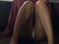 Close-up photograph of DeeannMilloy's legs, sitting with knees bent and slightly apart on a dark surface. Skin is smooth, highlighted by shadows. DeeannMilloy wears a sheer, pink fabric. Sexual tension.