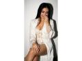 MiilaWx with long black hair, wearing a white lace lingerie dress and robe, sitting, covering her mouth with one hand, showing her tits and smooth legs.