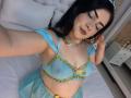 MadissonJoe with blue eyes, dark hair, and makeup, wearing a see-through blue and gold bra and skirt, showing her tits, lying on a bed, taking a selfie.