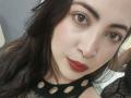 AlanaWest with pale skin, dark brown eyes, and red lipstick, wearing a black mesh top with circular cutouts, has long black hair and a slight smile.