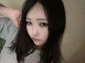 MarthaLipkind with long black hair, pale skin, and pouty lips, looking up with a slightly confused or bored expression, wearing a gray shirt, hand in hair.