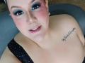 GiiannaMorrys has pink blush on her cheeks, blue eye makeup, a nose ring, and a tattoo on her shoulder. She's wearing a black polka dot top, showing her tits.