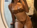 AmeliRoux with brown lace bra and matching panties, sitting on a black surface, holding her phone, showing her tits, ass, and pussy, with long brown hair and a necklace.