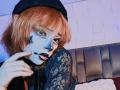 ViolettClay with orange hair, black beret, blue face paint, black lipstick, and lace top, sticking her tongue out, pointing to her mouth.