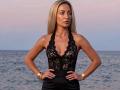 ViktoriiaLu with long blonde hair, wearing a black lace halter top that shows her tits, hands on hips, gold bracelet, and watch, standing in front of a ocean.