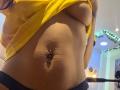 AfroditaWild's yellow shirt lifted, exposing her bare boobs and a pierced belly button with a jewelry piece. She's wearing dark lace panties, showing a slightly textured midsection.
