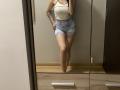 Olieri's tits are small, she's wearing a white crop top and blue tie-dye shorts, standing in front of a mirror, showing her tattooed arm and bare legs.