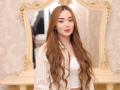 JaneKrover has long, wavy brown hair, wearing a white crop top and striped shirt, with a mirror and ornate frame in the background. She's smiling softly.