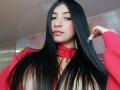NaiaSanders with long black hair, red hoodie, nose ring, and pink lips, holding hair, showing off her tits, cute, with a slight smirk.
