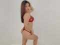 Julhiana with long brown hair, red lace bra, and red thong, standing sideways, showing her ass, smiling, hand in hair, white background, confident, sexy.
