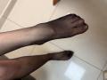 Tattiya's black sheer-clad foot is in the air, showing her toes and slightly curved pinkish toenails, with her other foot on the tiled floor below.