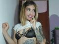 Kaiix with blonde hair, nose ring, and tattoos, lifting a white shirt to reveal leopard-print bra, teasing with finger on lips, showing off her small, perky tits.