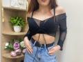 Rioria has small tits, wearing a black sheer off-shoulder top, blue denim jeans with a black belt, hands in pockets, brown hair, red lipstick.