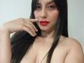 MadissonFontaine with long black hair, red lipstick, and a finger near her slightly parted red lips, showing her bare tits and pale skin. She has a small beauty mark.