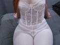 SheritaChieng's white lace corset and sheer panty set, showing her pale skin, small tits, and thick, white thighs, sitting on a grey bed with black pillow.