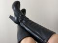 AlicePrings' black, high-heeled, leather boots with a zipped front, crossed at the ankles, showing her pale, bare thighs. Boots are shiny and slightly wrinkled.