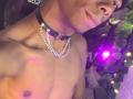 Shirtless MasterXx with dark brown skin, black leather choker with silver chain, and nose ring, smiling slightly, visible chest and nipples, purple and yellow lights in background.