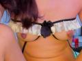HarlyMia's small, bare tits with dark nipples are visible above a black and white frilled bra, sitting with her dark brown hair partially in frame.