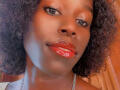 KharlaQueen's face with shiny red lipstick, dark curly hair, and a slight smile. She's wearing a silver chain necklace. Her brown eyes are looking directly at the camera.