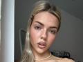 ArnettaNazario has blonde hair, blue eyes, and a pearl necklace, with a nose ring and slightly parted pink lips. Her tits are small and her face is cute.