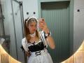 Hilaria Tabar, vêtue d'un uniforme de femme de chambre français noir et blanc avec un bandeau en dentelle blanche, tenant un téléphone, dans un autoportrait devant un miroir, montrant sa poitrine et un joli visage..