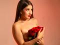 EmmaLombardi with red roses, holding them against her bare tits, long brown hair, red lipstick, pearl earrings, soft light, slightly smiling, looking to the side.