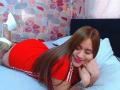 BelletinaXx, laying on a bed, red sports dress, long brown hair, white sneakers, smiling, butt raised, tattoo on right arm, head on hand, pink lipstick, relaxed, cute.
