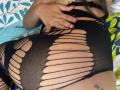 SharonKlart's black mesh outfit with large horizontal slits, exposing her tan skin and red-painted nails, resting her hand on her curvy ass. Visible tattoo on her right thigh.