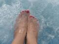 AmmyShtones' feet in clear water, toes painted bright red, toes slightly parted, water splashing around, wet skin, visible toes, relaxed posture.