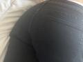 Sloaneswan's black, tight, denim-ass is facing the camera, showing the back pockets and the curve of her butt. The bed is slightly visible in the background.