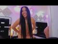 SiennaTaylor is nude, smiling, with long black hair, and large tits, standing with hands on hips, in a room with black tufted chairs and pink lighting.