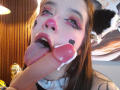 AryButty with pink nose, heart makeup, and cat ears, tongue out, licking a dildo with cum on it. She has pink eyeshadow, long eyelashes, and brown hair.