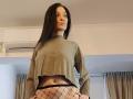 JoliDanielle with long black hair, wearing a green crop top and black fishnet panties, exposing her belly button and a small tattoo on her left side.