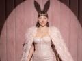 VeronikaGoldy has pink feathers on her shoulders, a sparkly pink corset, and pigtails, with a shadow of bunny ears on the pink wall behind her.